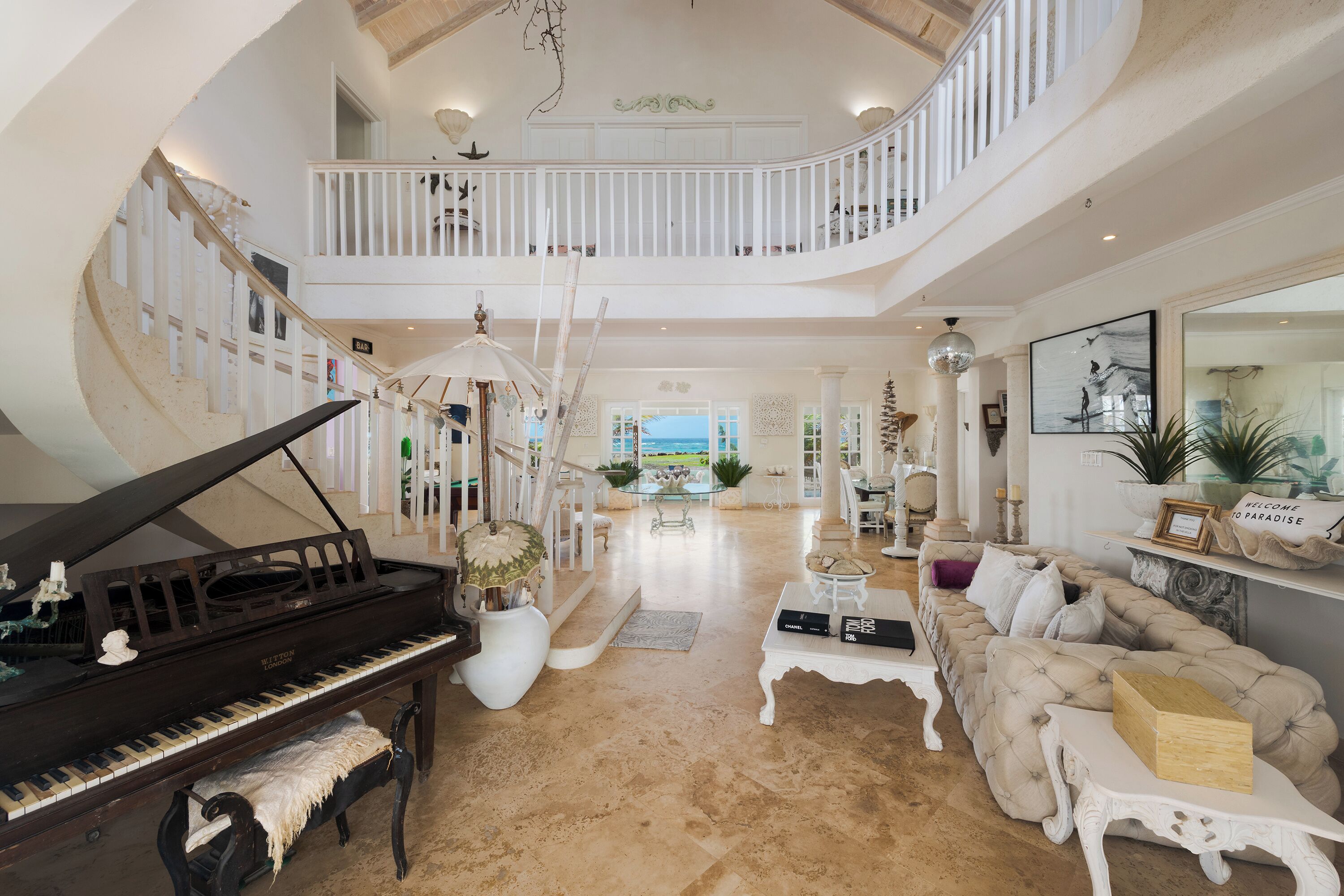 A spacious living area with a grand piano, a high-ceilinged staircase, and a view of the outdoors.