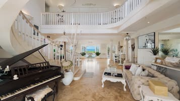 A spacious living area with a grand piano, a high-ceilinged staircase, and a view of the outdoors.