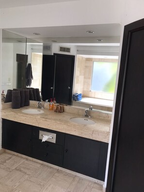 Une salle de bain moderne dotée d’un double lavabo, d’un grand miroir et d’une fenêtre laissant entrer la lumière naturelle.