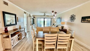 A dining area with a wooden table and chairs, a ceiling fan, and a view of the outdoors through a sliding door.