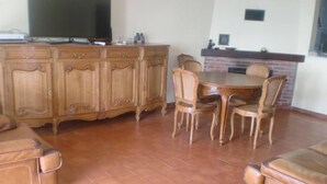 A living room with a wooden cabinet, a TV, a fireplace, and a dining area with chairs.