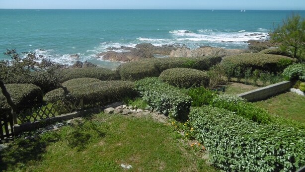 A coastal landscape with a view of the sea, rocky coastline, and well-maintained hedges.