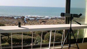 A telescope on a balcony overlooking a rocky coastline.