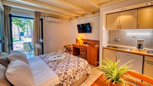 A hotel room with a bed, a desk with a chair, a TV, a kitchenette, and a view of the outside. - 3 * apartments / 2pax studio (Zaton)