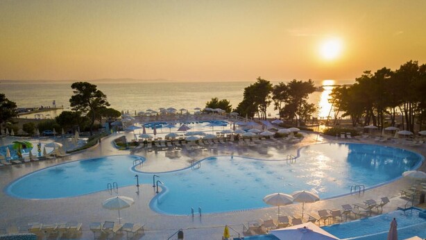 A large, multi-level swimming pool with sun loungers and umbrellas, surrounded by palm trees and overlooking the sea. - 3 * apartments / 2pax studio (Zaton)