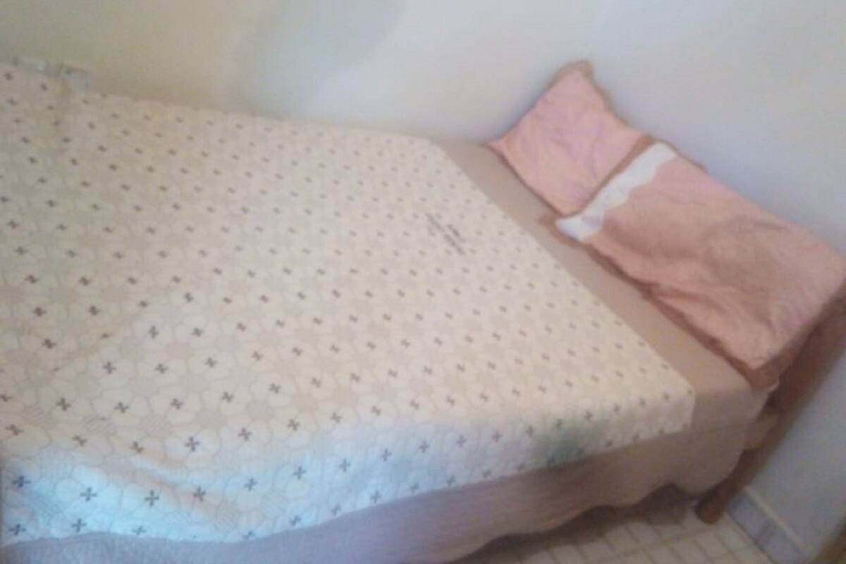 A small, single-bed room with a patterned bedspread and a pink pillow.