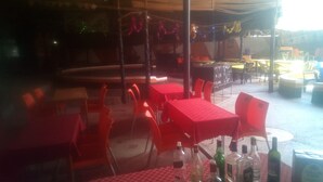 An outdoor dining area with red tables and chairs, a covered seating area, and various bottles on tables. - Comfy Bar And Restaurant (Nairobi)
