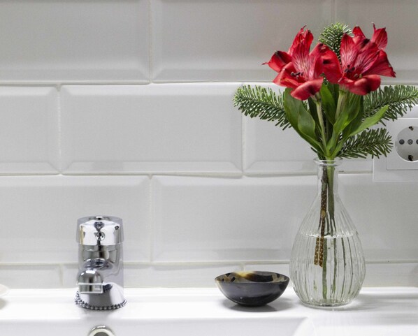 A bathroom with a white tiled wall, a clear glass vase with red flowers, a black bowl, and a chrome faucet.