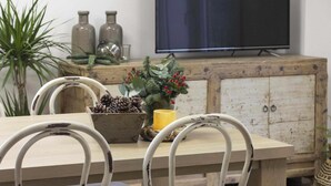 Un comedor con una mesa de madera, sillas de metal blanco y un televisor al fondo.