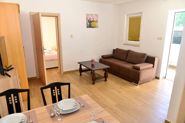 A living room with a brown sofa, a wooden coffee table, and a dining table set with plates and glasses.