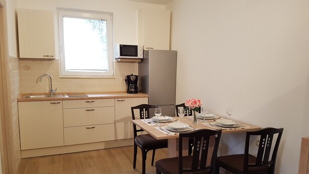Una cocina compacta con un lavamanos, microondas y refrigerador. Hay una mesa de comedor con sillas y un jarrón de flores.