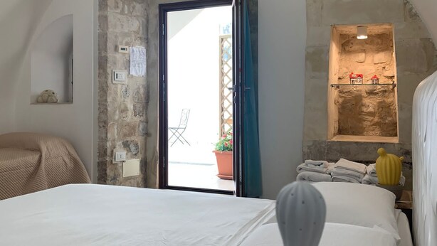 A bedroom with a bed, a potted plant, and a stone wall. - Aristogatti (Ragusa)