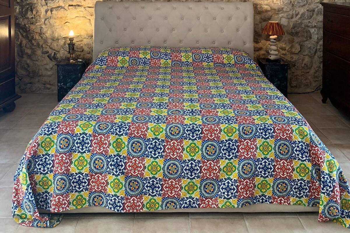 Un dormitorio con pared de piedra, cabecera capitoneada, colcha estampada y dos mesitas de noche con lámparas.