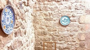 A dining table set with plates, glasses, and a teapot, against a stone wall with decorative plates. - Aristogatti (Ragusa)