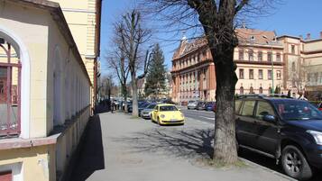 A street with parked cars, a yellow car in the foreground, and buildings with arched windows on the left.