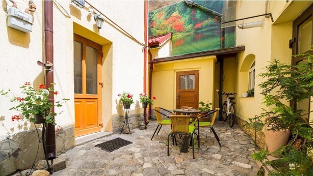 Un patio con piso de piedra, una puerta de madera, una mesa con sillas y plantas en macetas.