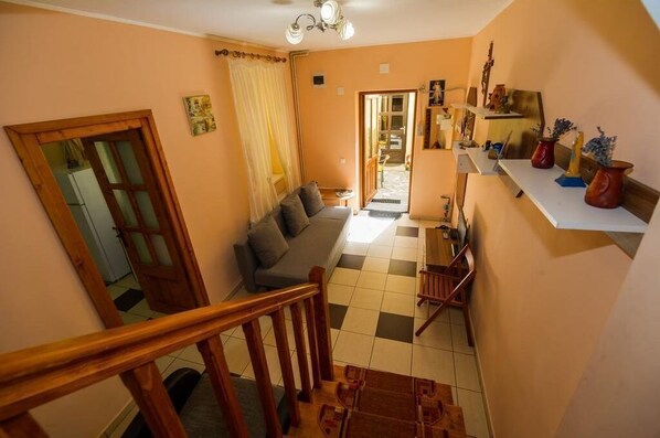 Un escalier mène à un espace de vie comprenant un canapé, une table à manger et une cuisine visible à travers une porte ouverte.