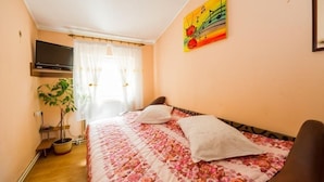 Un dormitorio con cama, televisor, planta y un cuadro en la pared.