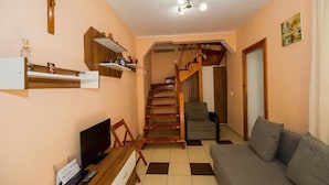 Una sala de estar con sofá, televisor, estanterías de madera, una escalera y una puerta.