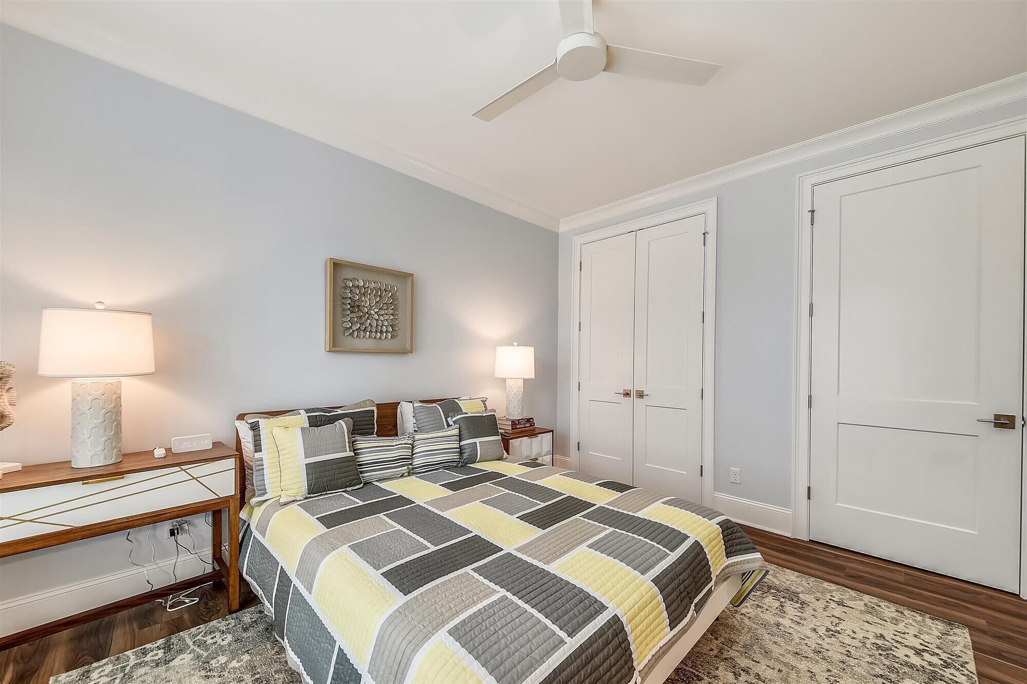 A bedroom with a bed, two bedside tables, a nightstand, a ceiling fan, and two wardrobes.
