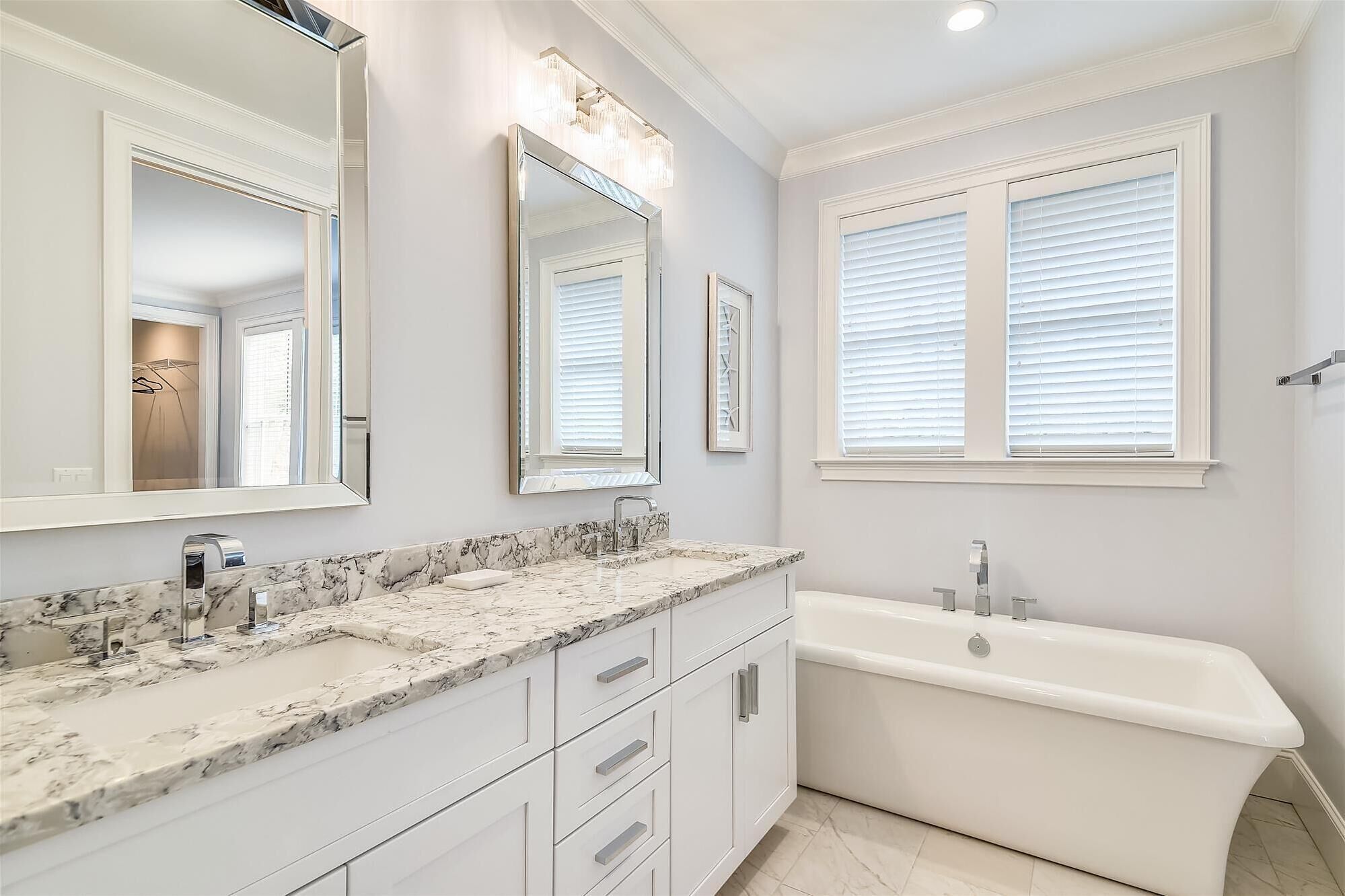 A bathroom with a marble sink, a large mirror, a bathtub, and white window blinds.