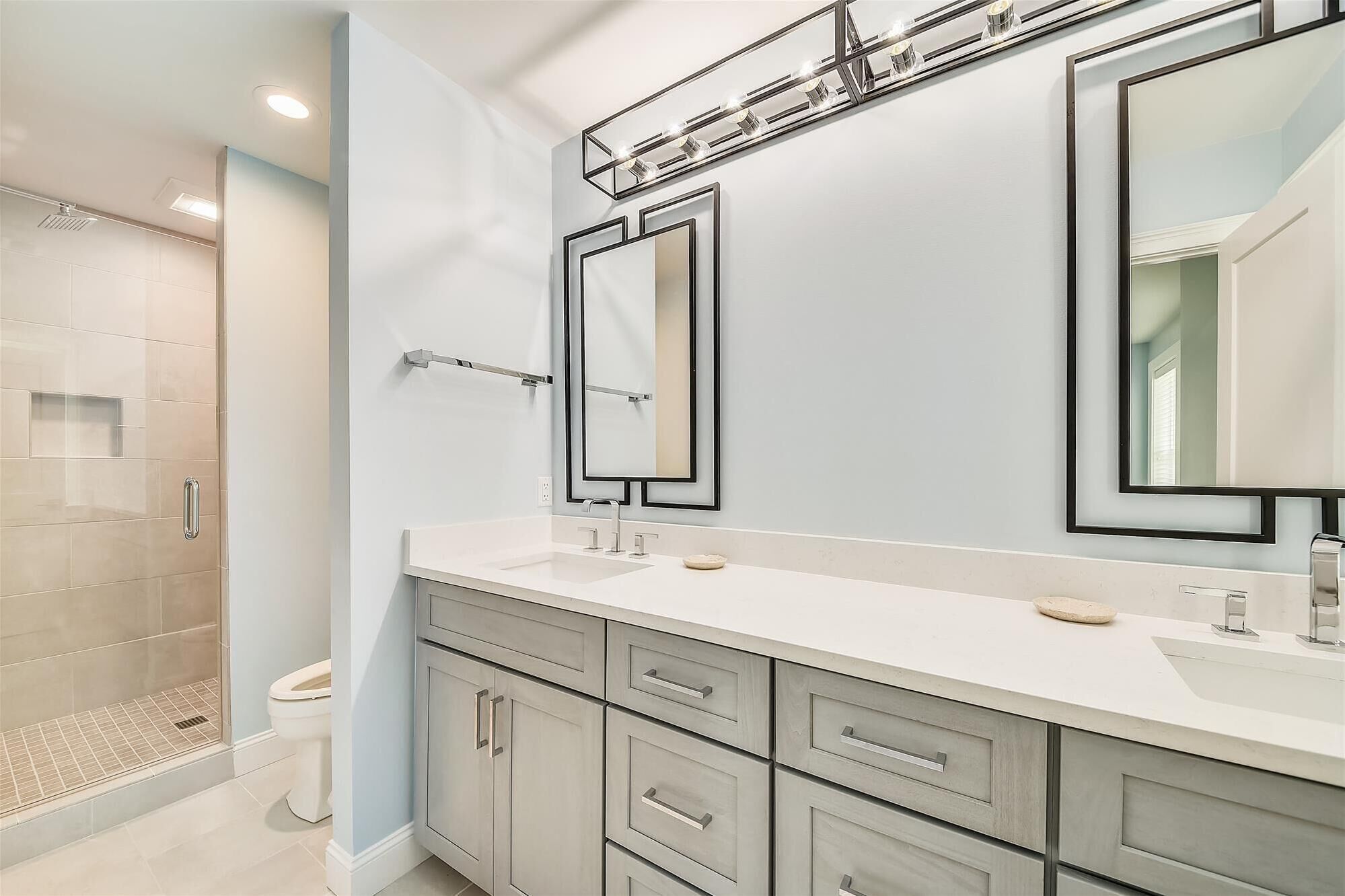 Un baño moderno con cabina de ducha, tocador doble con un espejo grande y un inodoro.