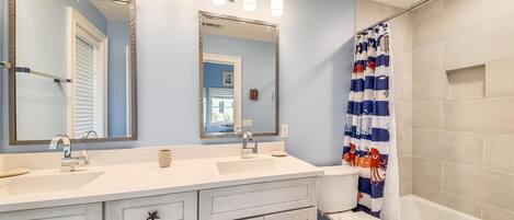 A bathroom with two sinks, a toilet, and a bathtub. There are three mirrors above the sinks, and a shower curtain with a fish pattern.