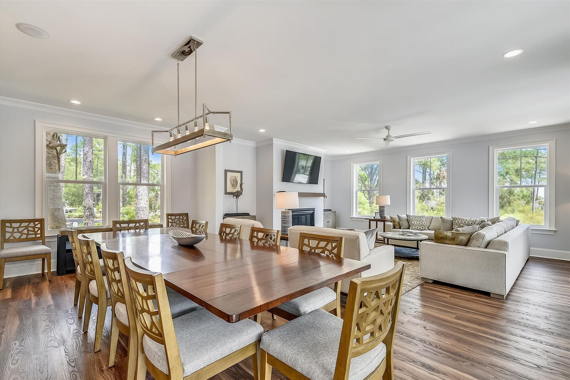 A spacious living room with a wooden dining table, comfortable seating, a fireplace, and large windows offering a view of the outdoors.