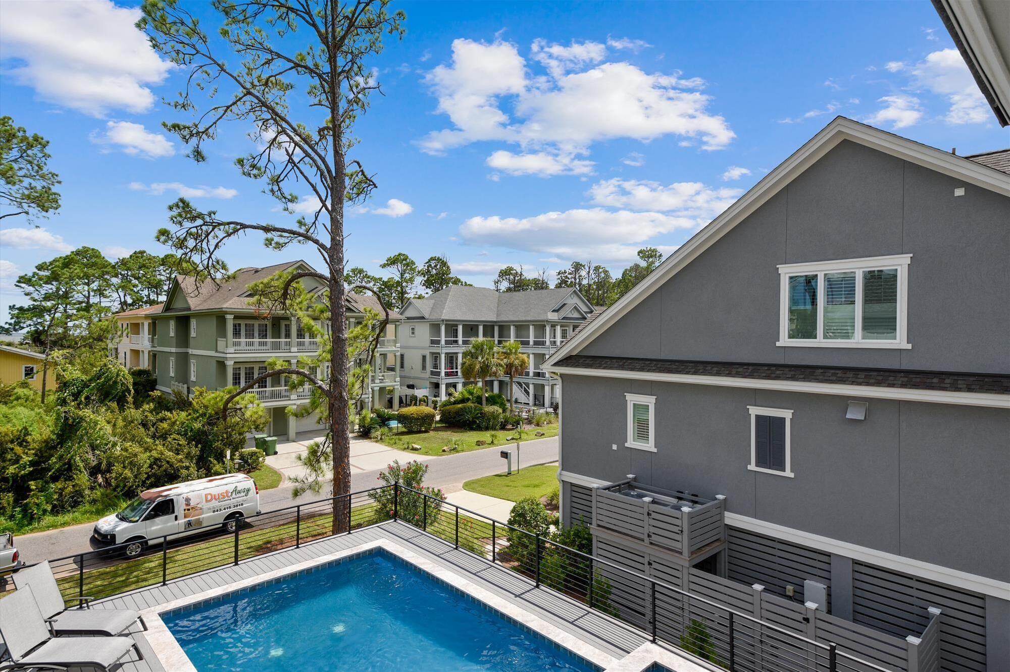 A residential area with a swimming pool, a grey house, and a white van parked nearby.