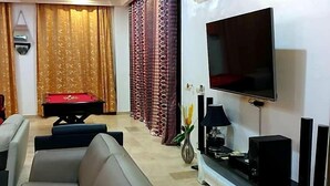 A living room with a sofa, a billiards table, a flat-screen TV, and an air conditioning unit. - Have'Den Resort-Hôtel (Abidjan)