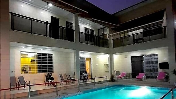 A swimming pool with a red rope barrier, lounge chairs, and a two-story building with balconies. - Have'Den Resort-Hôtel (Abidjan)