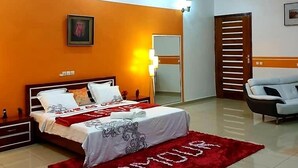 A modern bedroom with a bed, a red rug, a sofa, and a mirror. - Have'Den Resort-Hôtel (Abidjan)