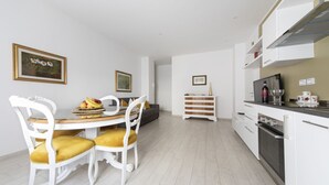 Una cocina moderna con armarios blancos, un comedor con mesa blanca y sillas amarillas, y un sofá gris.
