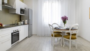 Cocina moderna con armarios blancos, un refrigerador de acero inoxidable y un comedor con mesa y sillas blancas.