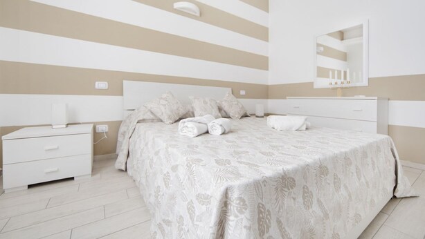 Un dormitorio con diseño de pared a rayas, una cama con cubrecama floral, una mesita de noche con lámpara y un espejo sobre la cama.