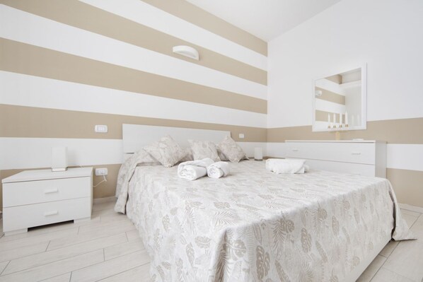 A bedroom with a bed, bedside tables, a mirror, and a wall-mounted light fixture.