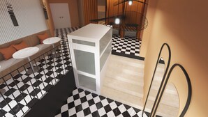 Una habitación de hotel moderna con suelo de cuadros, un sofá con cojines, una mesita, un armario blanco y un comedor con candelabro.