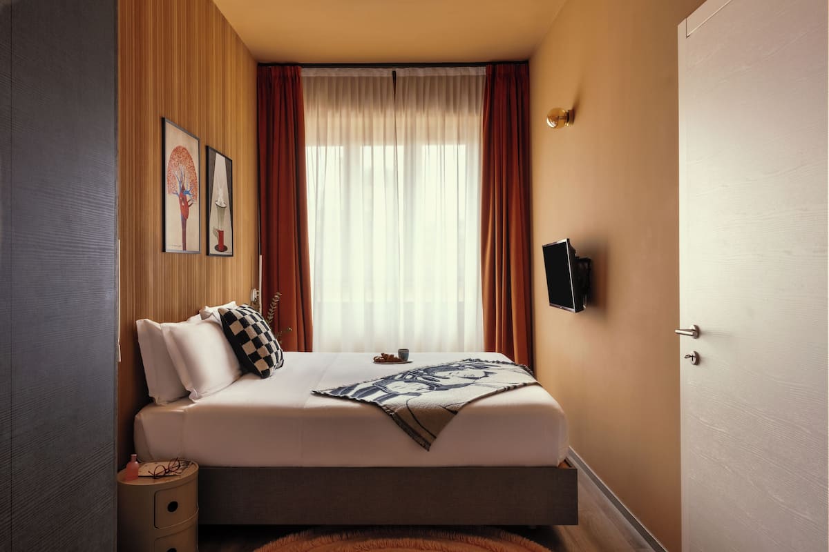 Un lit bien fait, avec une couverture, une table de chevet avec une lampe et un téléviseur fixé au mur.