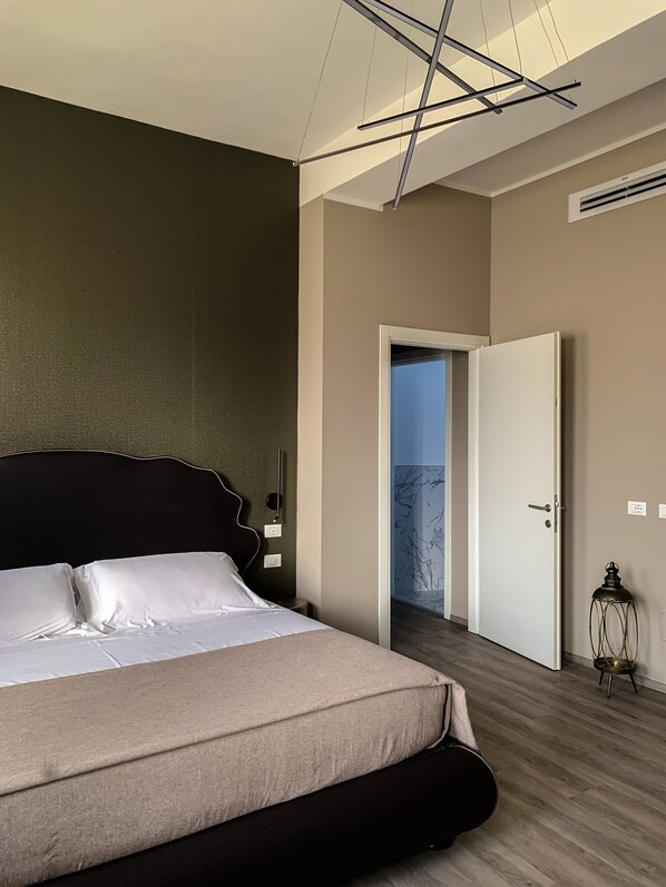 A modern bedroom with a large bed, a nightstand, a wall-mounted light, and a door leading to another room.