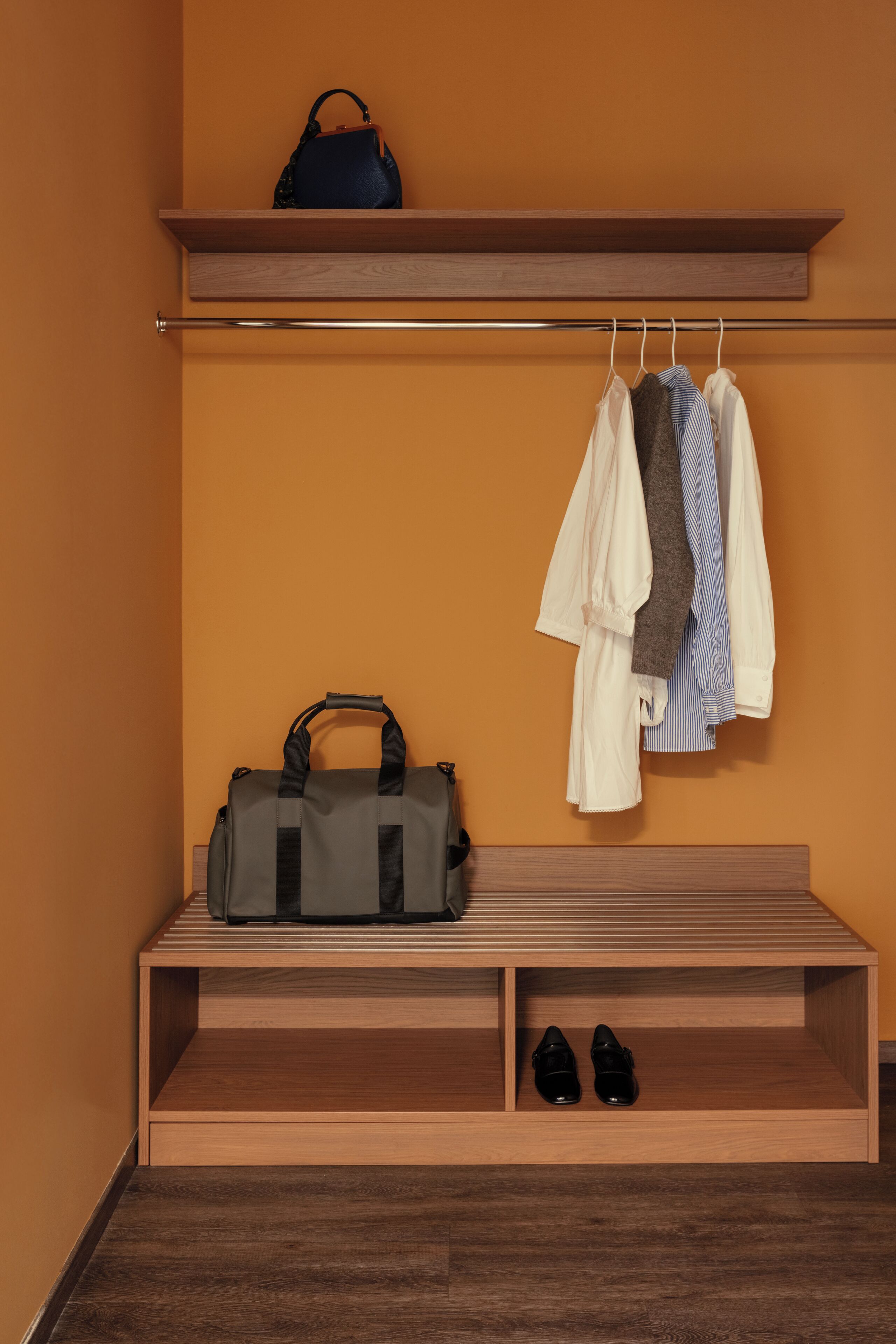 Um banco de madeira com uma bolsa e sapatos, um cabide com roupas e uma prateleira com uma sacola.
