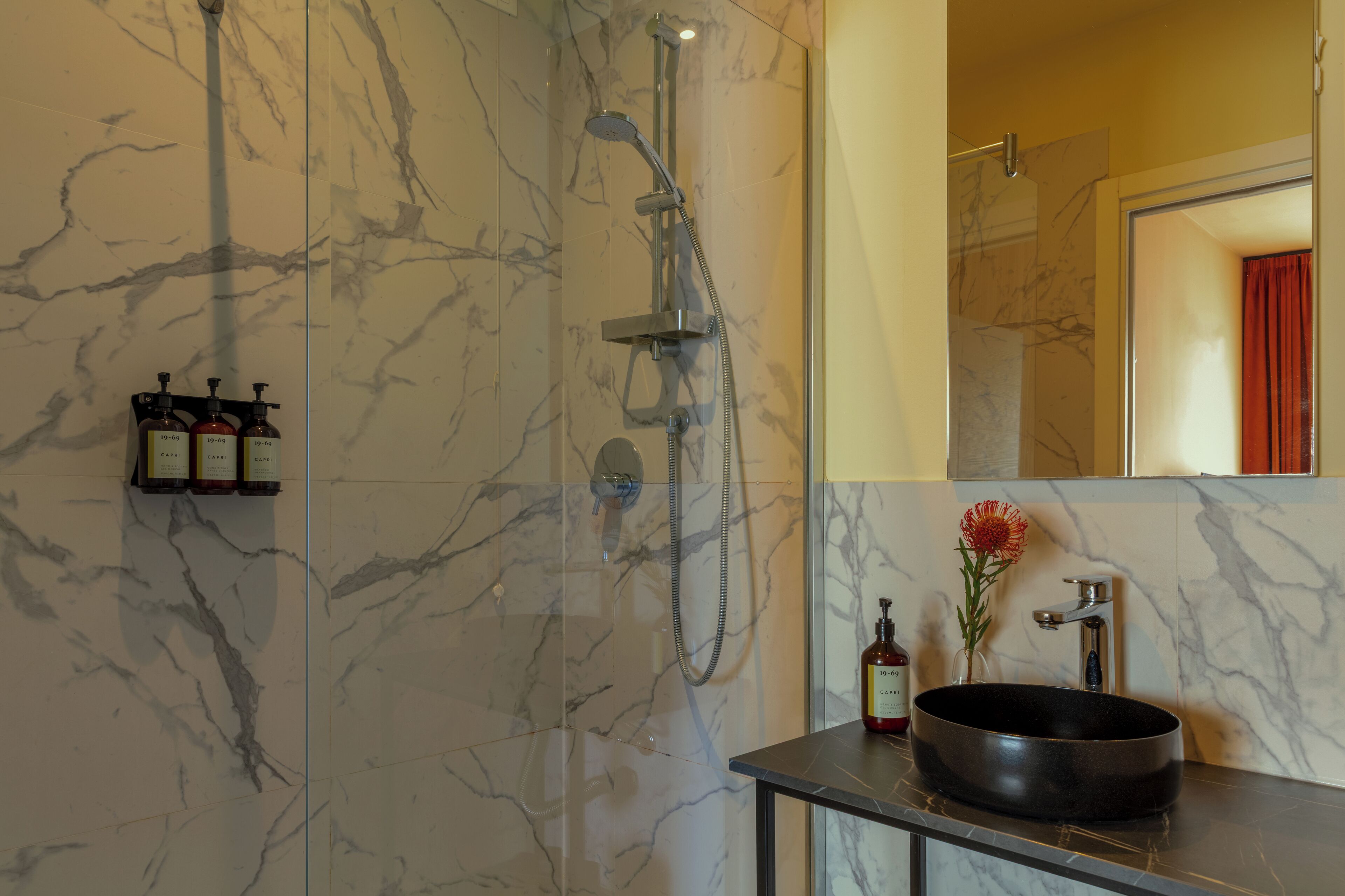 A bathroom with a marble wall, a black sink, a mirror, and a shower.