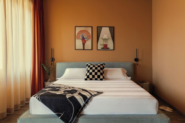 Una cama bien hecha con un cojín de cuadros, una manta estampada y dos cuadros enmarcados en la pared.
