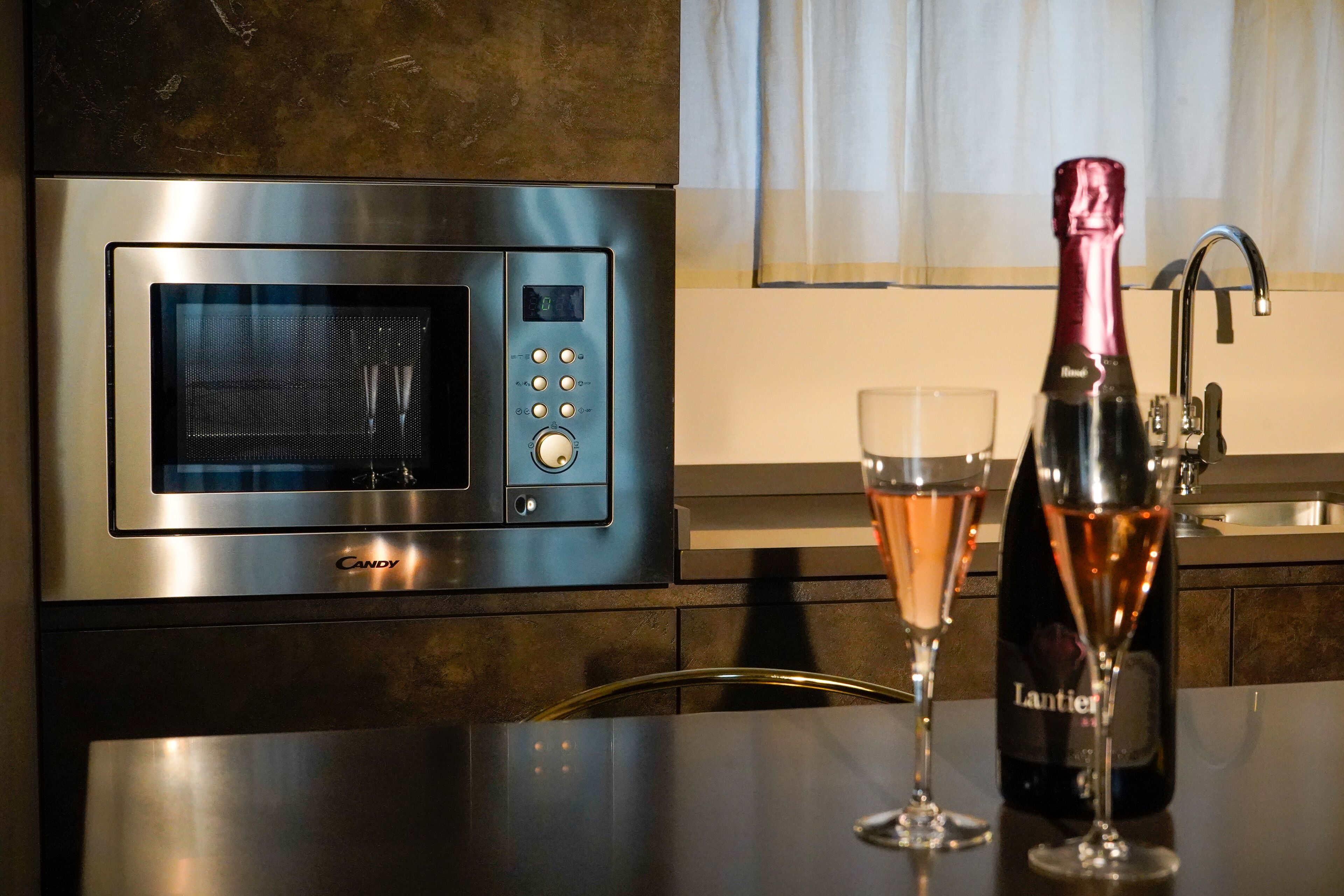 Une cuisine équipée d’un four à micro-ondes moderne, avec une bouteille de vin et deux verres posés sur le comptoir.