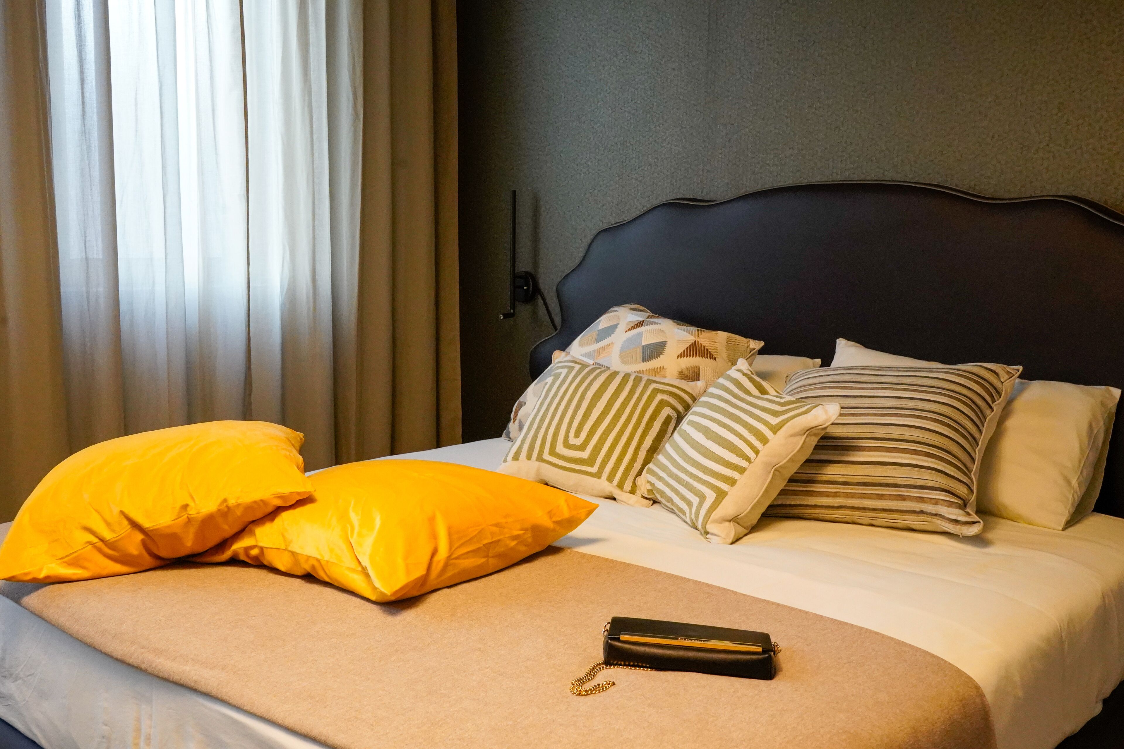 Una habitación de hotel con cama, almohadas, una mesita de noche y un velador.