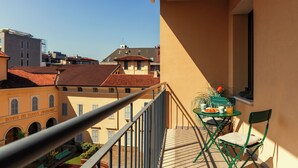 Un balcón con mesa y sillas, con vista a un paisaje urbano de edificios y cielo despejado.