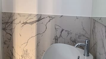 Un baño con lavamanos blanco, paredes de mármol y suelo de madera.