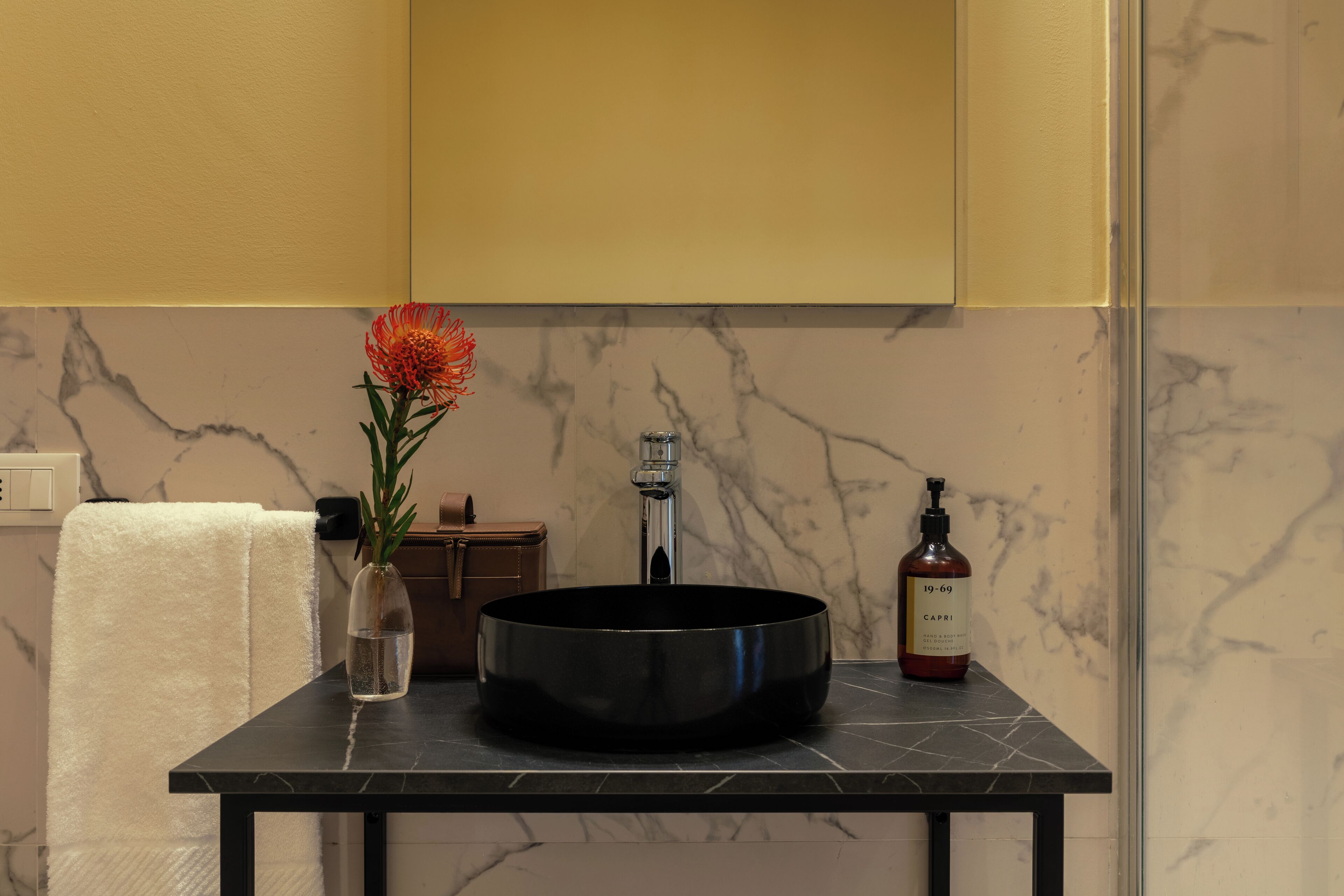 A bathroom with a marble sink, a towel, a vase with a flower, and a bottle of hand soap.
