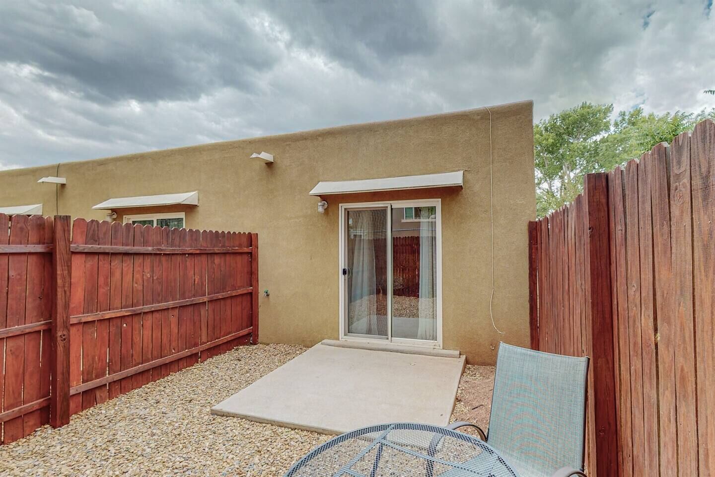 A residential backyard with a wooden fence, a patio area, and a sliding glass door leading to a covered patio.