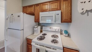 A compact kitchen with wooden cabinets, a white refrigerator, a microwave, a stove, and a coffee maker. - Mountain Road Hideaway, near Old Town (Albuquerque)