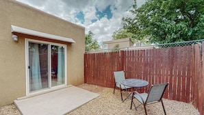 A patio with a table and chairs, a wooden fence, and a building with a sliding glass door. - Mountain Road Hideaway, near Old Town (Albuquerque)